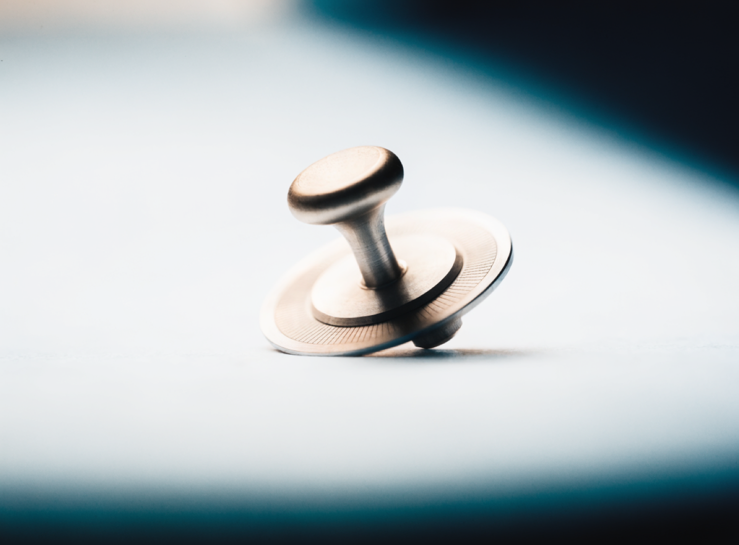 A single warm-lit machined dial with fine engraved graduations, resting slightly tilted in a cool field — a small human touchpoint among precision instruments.