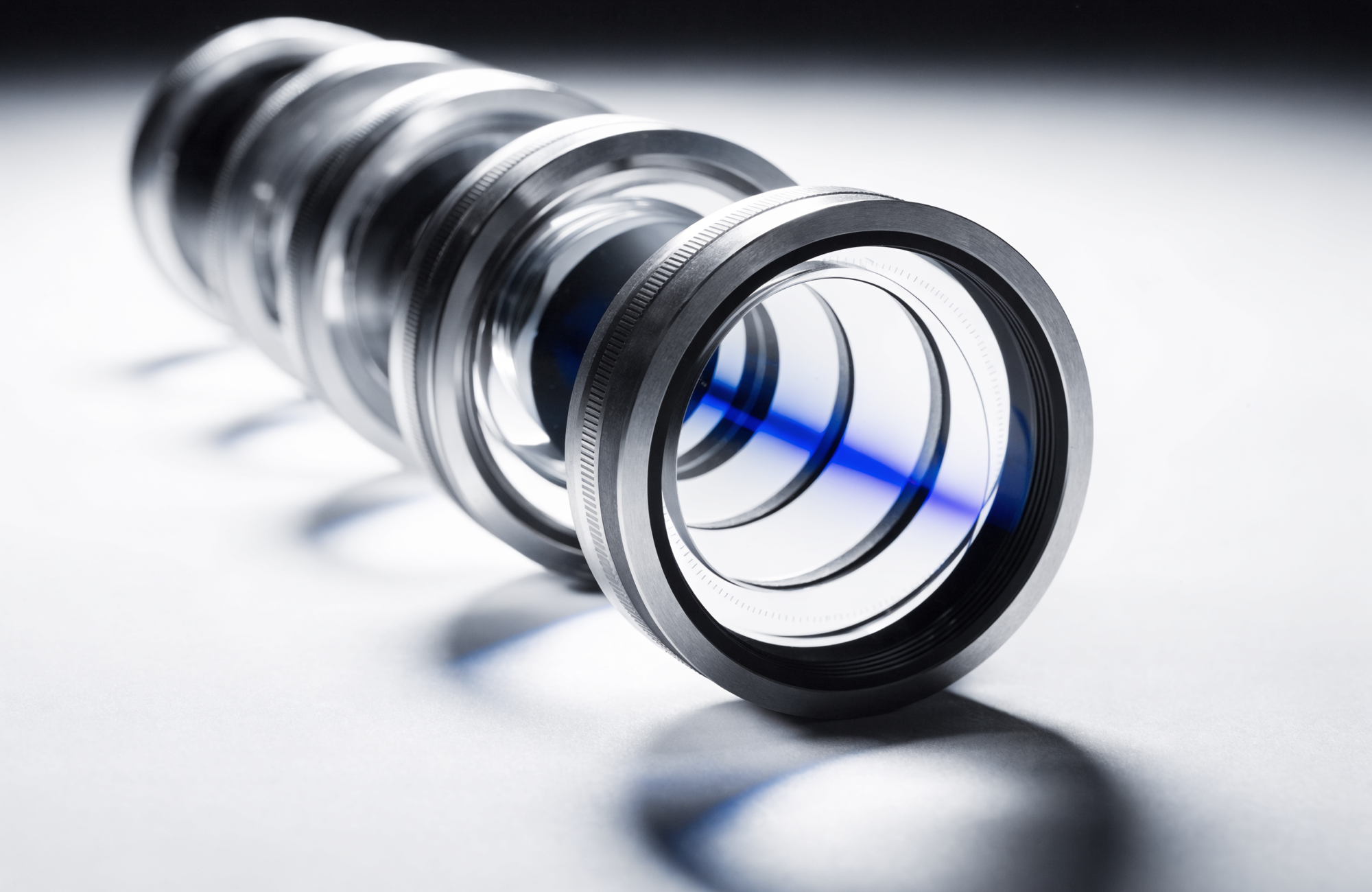 Looking straight down the axis of a machined lens assembly, concentric rings drawing the eye to a bright cobalt-blue core of light at the centre.